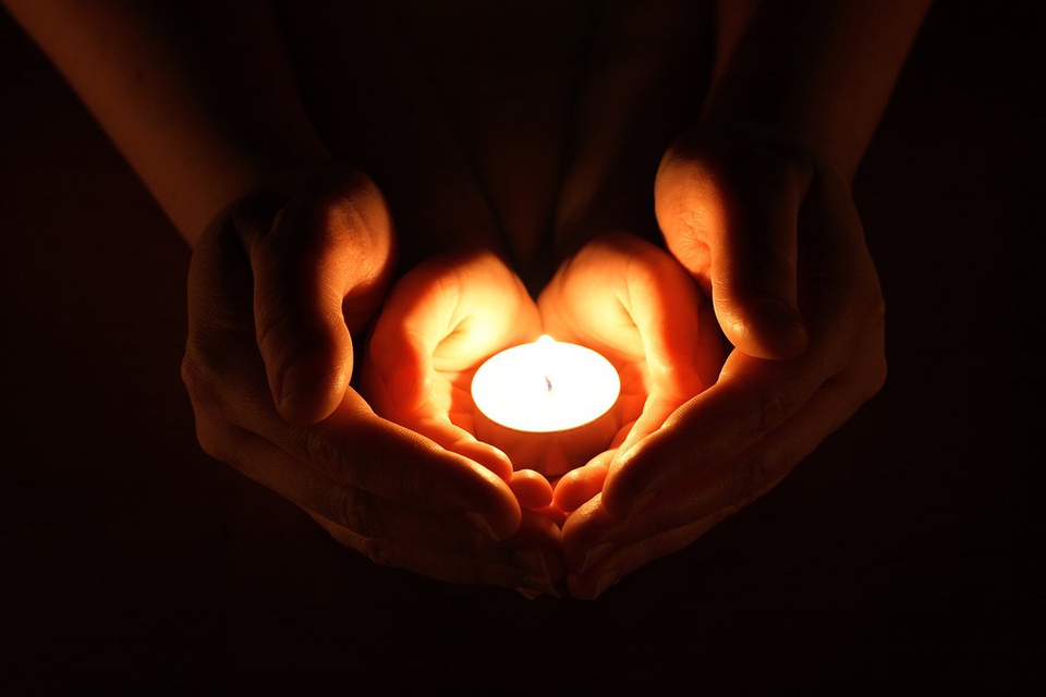 Hands held in prayer in the light of a candle