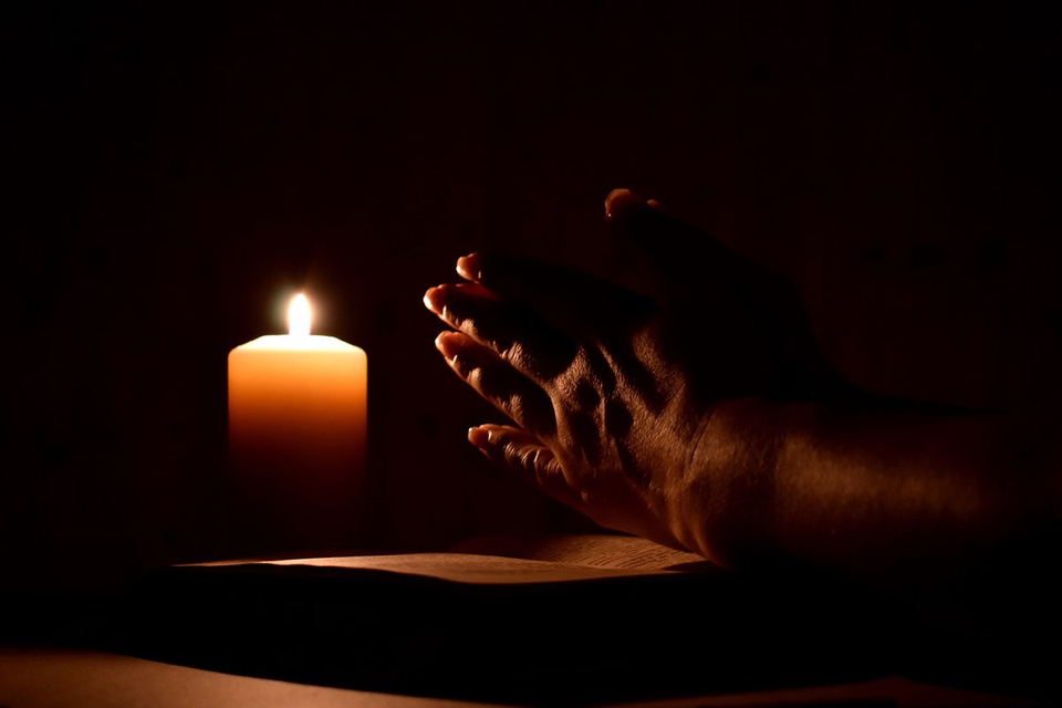 Hands held in prayer in the light of a candle