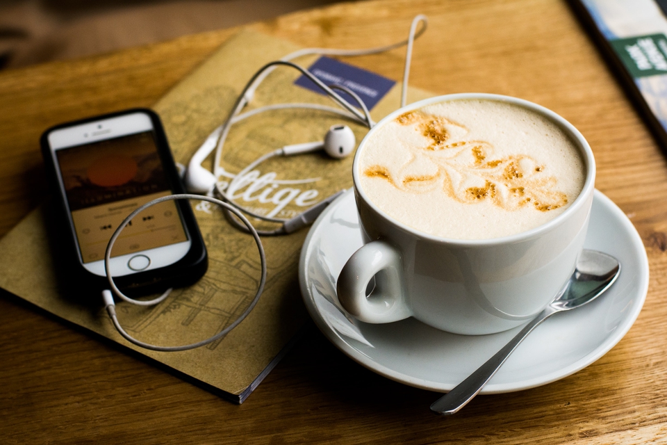 A cup of coffee with a phone and earbuds